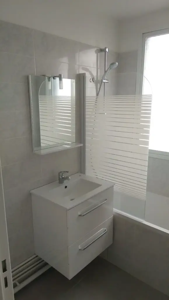 Baie finalizată cu gresie albă, lavoar și duș cu sticlă catifelată