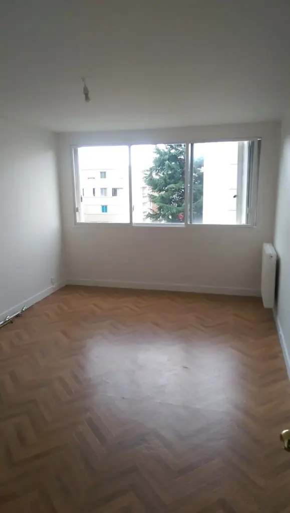 Cameră finalizată cu pereți albi, parchet și ferestre cu vedere de bloc