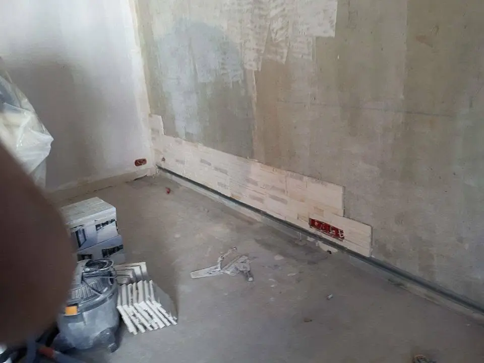 Perete baie cu gresie albă montată și bandă decorativă neagră, doze electrice instalate