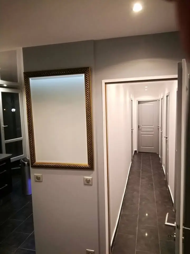 Cameră/living finalizată: canapea gri cu haine stivuite, scaune, masa rotunda, lampă, tablou pe