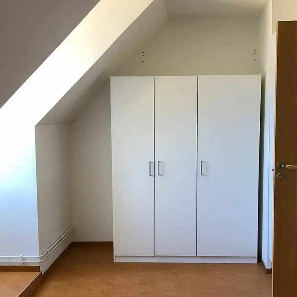 Cameră mansardă cu garderobă albă încorporată pe perete, pardoseală din lemn