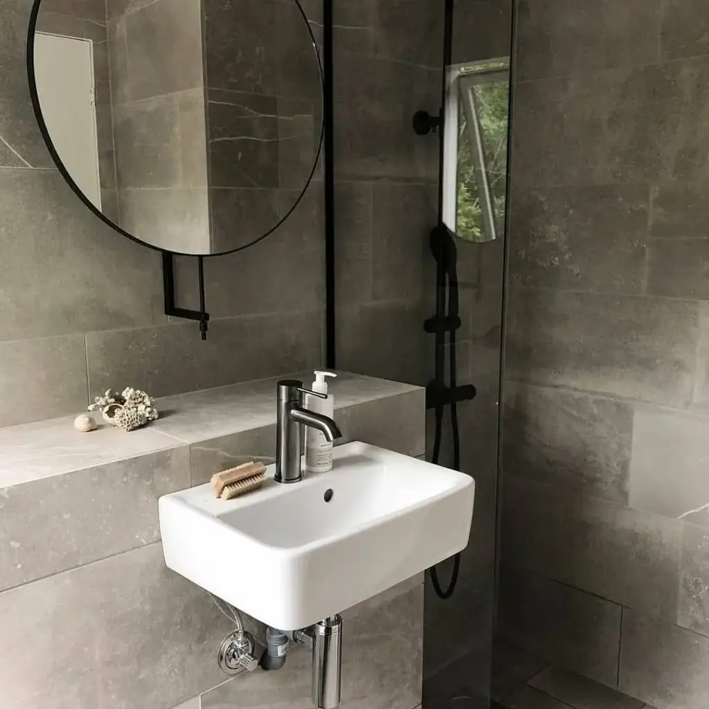 Baie cu gresie tip industrial, oglindă circulară modernă, chiuvetă suspendată albă, duș cu