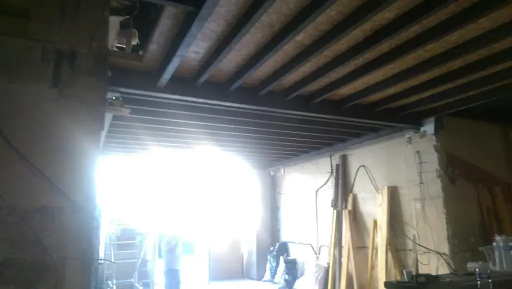 Spațiu cu grinzi de lemn pe tavan, cabluri electrice, praf, echipament de construcție