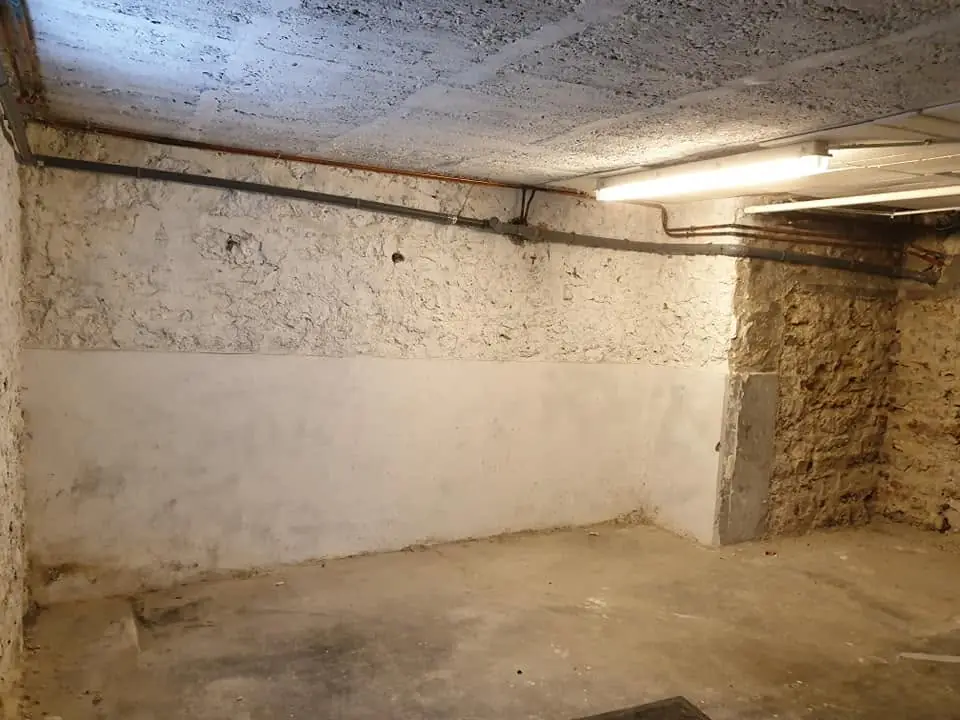 Subsol/cameră tehnică, beton brut + zugrăvire parțială (stânga), conducte sanitare expuse, iluminare neon